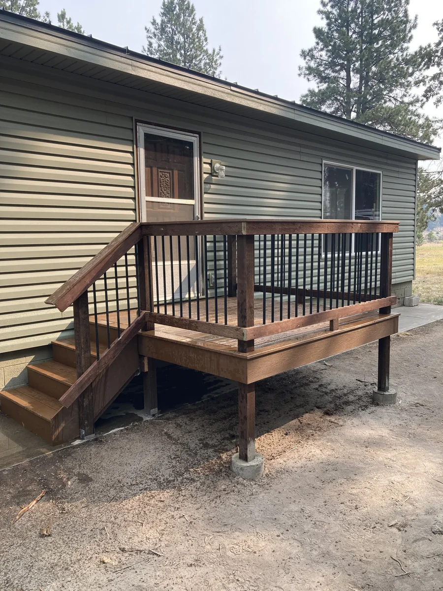 After deck installation showing expanded wood deck, stairs, and black railing at a Klamath Falls home